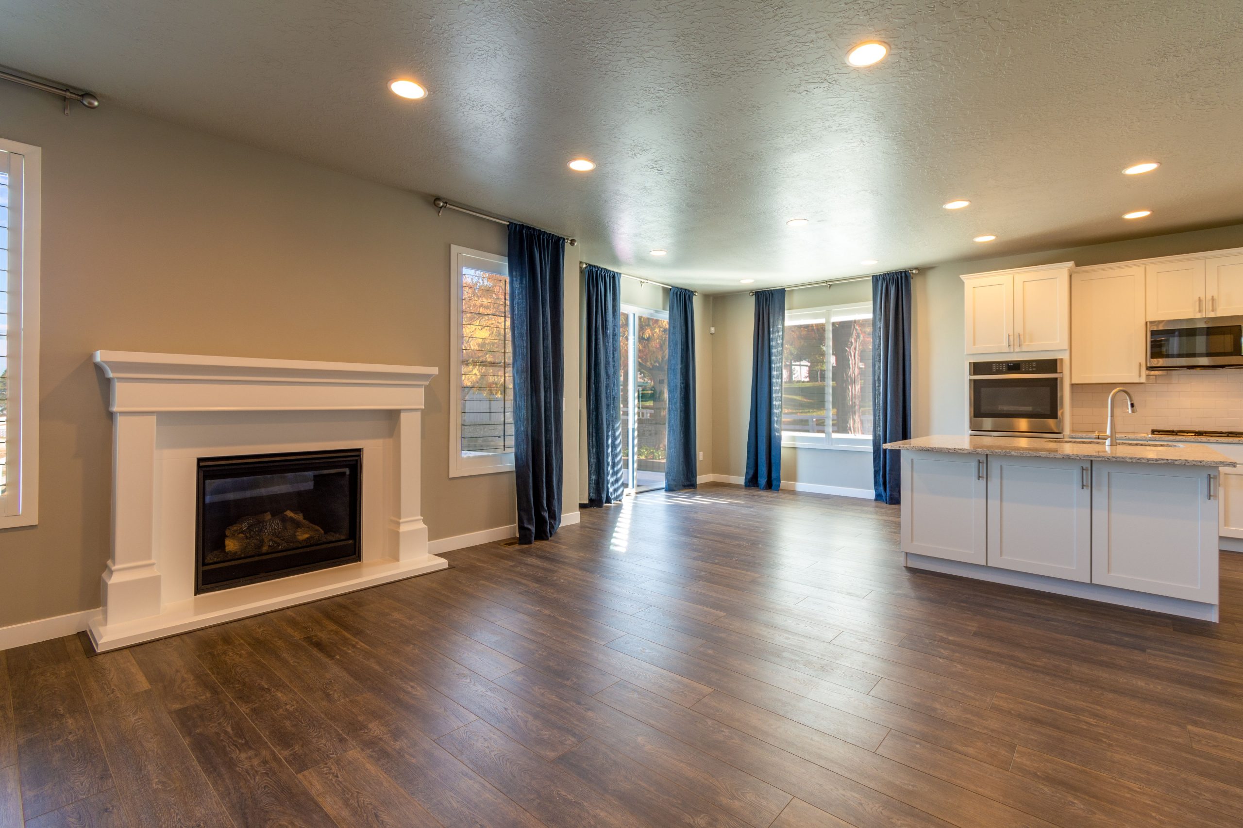 Dark walnut-toned hardwood flooring running from a fireplace through to the kitchen island in an empty open-plan Tennessee living room