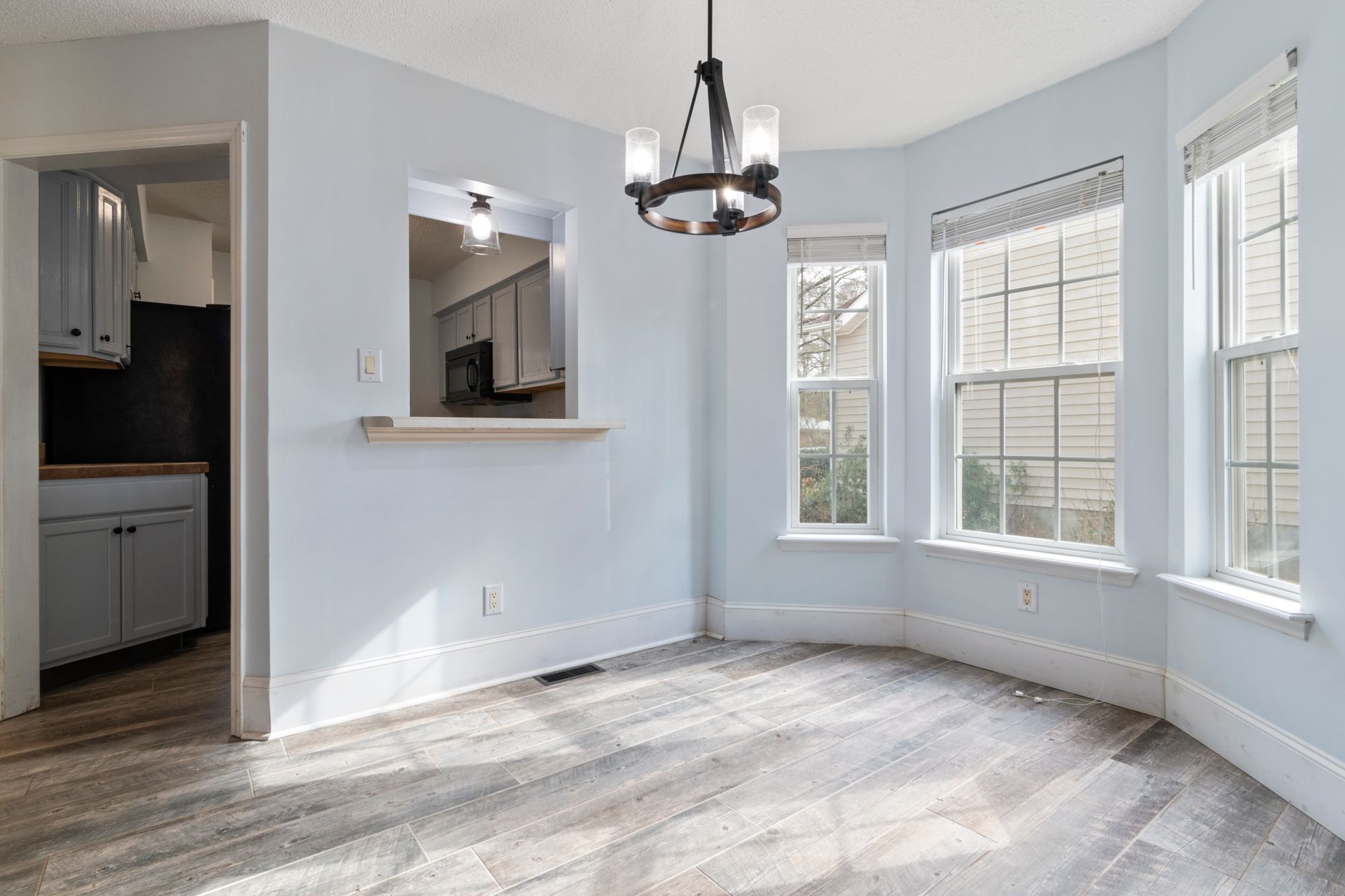 Sunlit empty room featuring a modern chandelier and wooden floors
