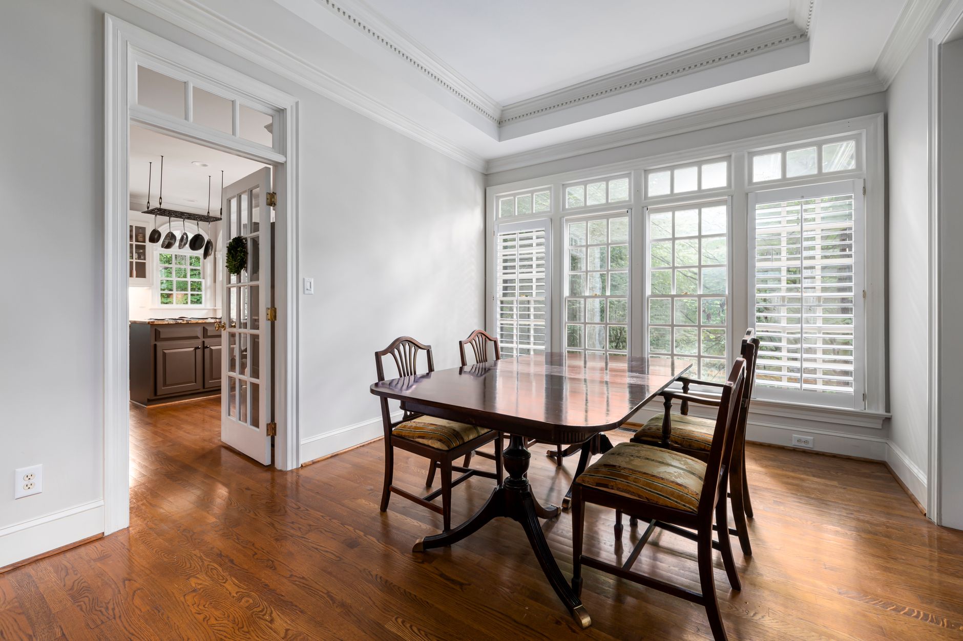Bright dining room featuring a wooden table, classic chairs, and large windows overlooking greenery